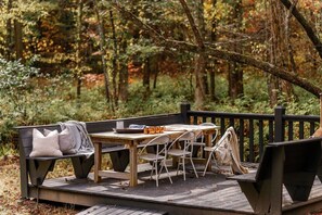 An outdoor deck with a wooden table and chairs, surrounded by a forest.
