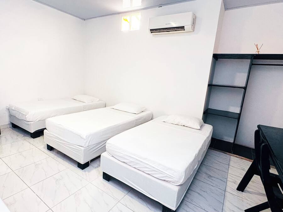 Quarto com duas camas de solteiro, uma mesinha, escrivaninha e estante.