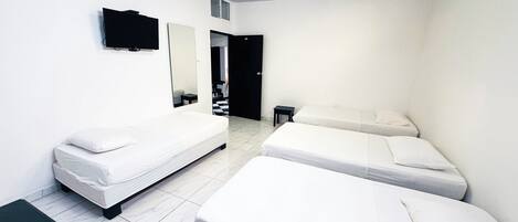 A hotel room with two single beds, a small table, a TV, and a mirror.