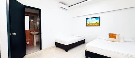A hotel room with a bed, a bedside table, a small stool, a sink, and a shower area.