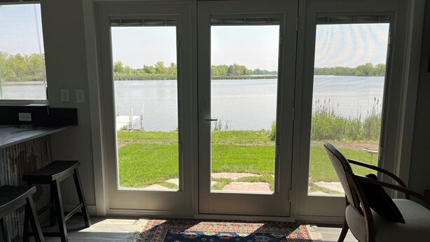 A room with a large sliding glass door leading to a lake view, a small bar area, and a patterned rug on the floor. - Rock River Retreat Boathouse Bungalow...Relax, Refresh, and Enjoy this Zen Den (Horicon)