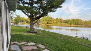 A stone pathway leading to a grassy area with a tree and a lake in the background. - Rock River Retreat Boathouse Bungalow...Relax, Refresh, and Enjoy this Zen Den (Horicon)