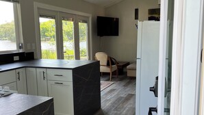 A modern kitchen with a marble island, white cabinetry, and a large window overlooking greenery. - Rock River Retreat Boathouse Bungalow...Relax, Refresh, and Enjoy this Zen Den (Horicon)