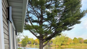 A stone pathway leading to a bench under a large tree, with a lake and houses in the background. - Rock River Retreat Boathouse Bungalow...Relax, Refresh, and Enjoy this Zen Den (Horicon)