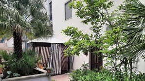 A courtyard with a palm tree, potted plants, and a striped awning. - Apartment in Matera near Historic Center (Matera)