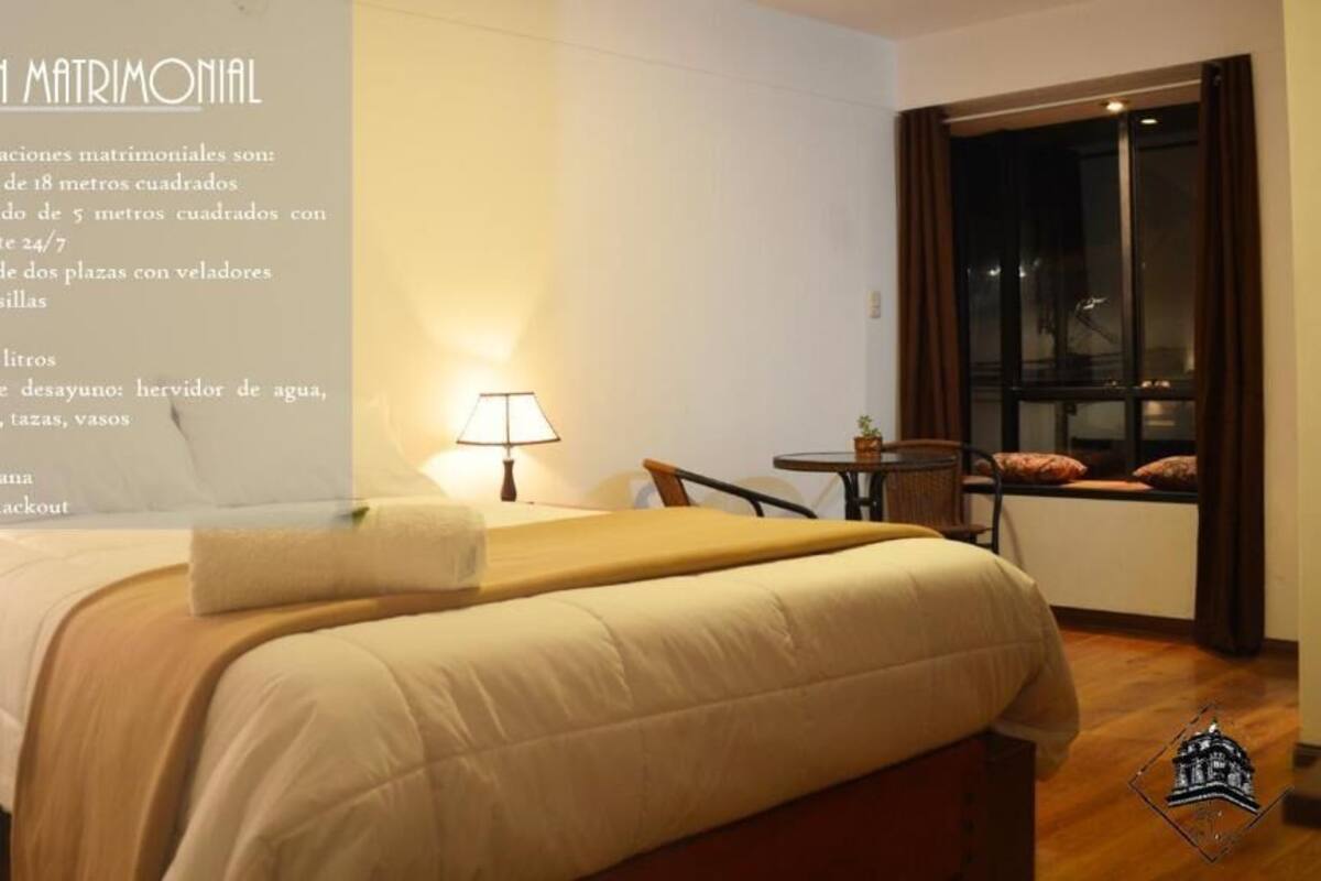 A modern hotel room with a large bed, a desk, a chair, and a window with curtains.