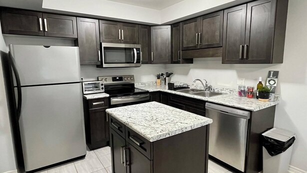 A modern kitchen with dark cabinets, stainless steel appliances, a granite countertop, and a tiled floor. - Niagara Getaway! 6 bedrooms , 4.5 baths. Up to 12 guests. Gameroom in Garage.  (Thorold)