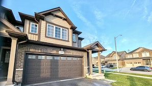 A two-story house with a garage, a covered porch, and a well-maintained lawn. - Niagara Getaway! 6 bedrooms , 4.5 baths. Up to 12 guests. Gameroom in Garage.  (Thorold)