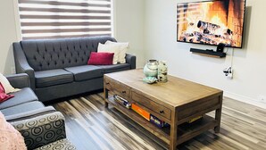 A living room with a grey sofa, a wooden coffee table, and a television mounted on the wall. - Niagara Getaway! 6 bedrooms , 4.5 baths. Up to 12 guests. Gameroom in Garage.  (Thorold)