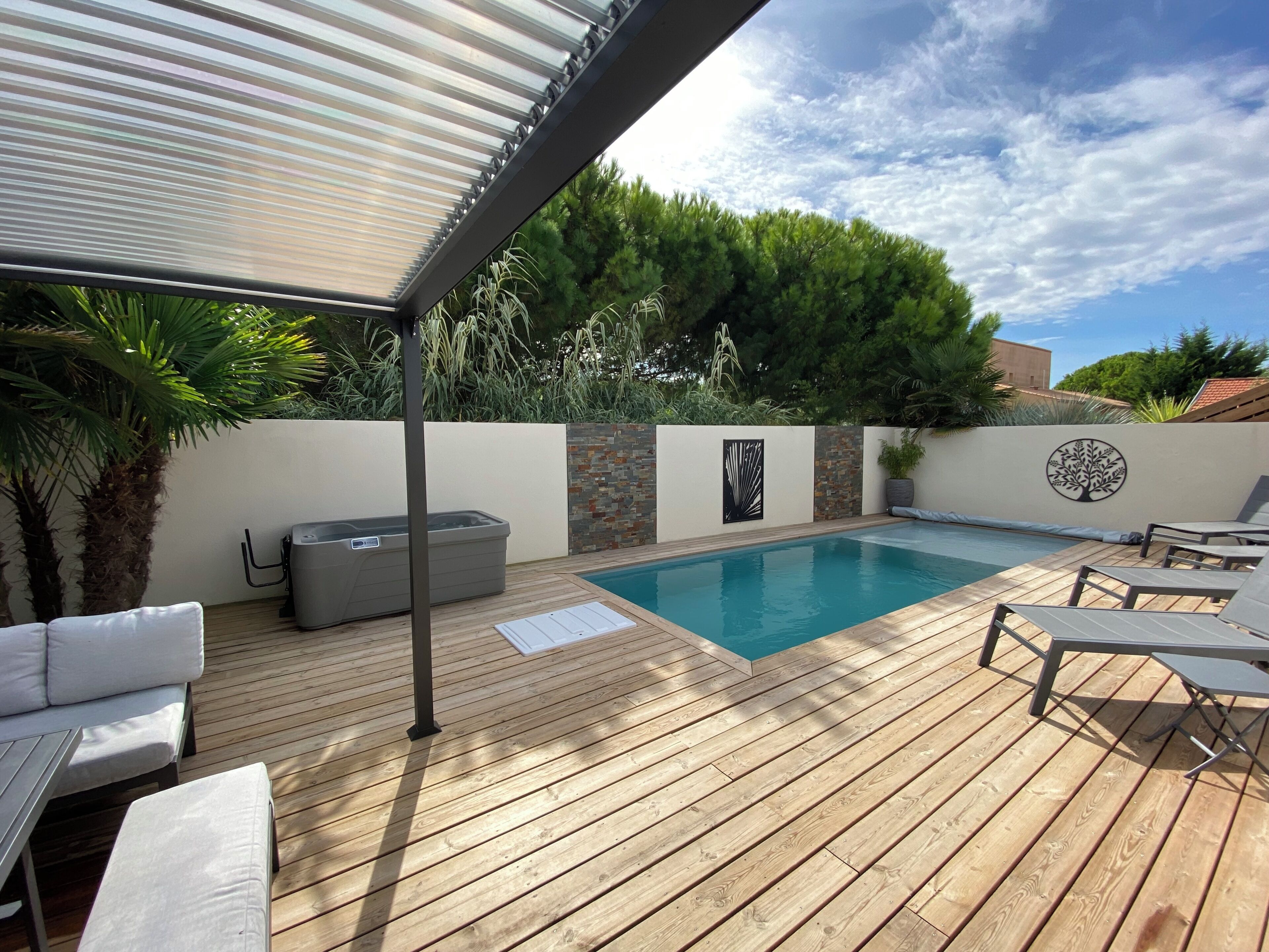 Una terraza de madera con piscina, sillas de descanso, bañera de hidromasaje y un pérgola.