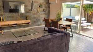 Una sala moderna con pared de piedra, un televisor de pantalla plana, una mesa de centro de vidrio, un sofá y una zona de comedor con sillas y una mesa.