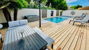 Una terraza de madera con piscina, sillas de descanso, un jacuzzi y un área de estar techada.