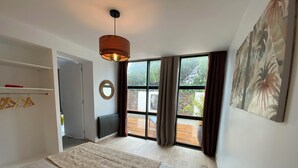 Un dormitorio con cama, un radiador, una ventana con cortinas, una lámpara colgante y un cuadro en la pared.