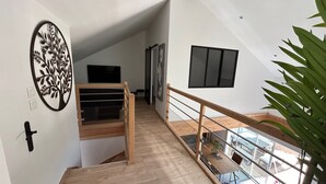 Una escalera moderna con escalones de madera y barandilla de vidrio, que conduce a un nivel inferior con un banco y un televisor de pantalla plana montado en la pared.