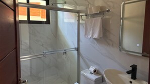 Un baño con cabina de ducha de vidrio, inodoro, lavamanos y perchero para toallas.