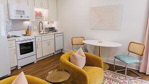 A compact kitchen with white cabinets, a microwave, a stove, and a coffee maker. There is a small round table with two chairs, one with a cushion. - NEW!! The Coop I Pettigrew Adventures in Midtown - Located in Cooper Young  (Memphis)