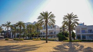 Una playa arenosa con palmeras y edificios modernos al fondo.