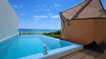 A clear blue infinity pool with a view of the ocean, a wooden deck, and a small tent-like structure.