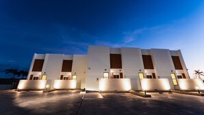 Un hotel moderno con una fachada simétrica, varios puntos de acceso iluminados y un amplio espacio exterior.