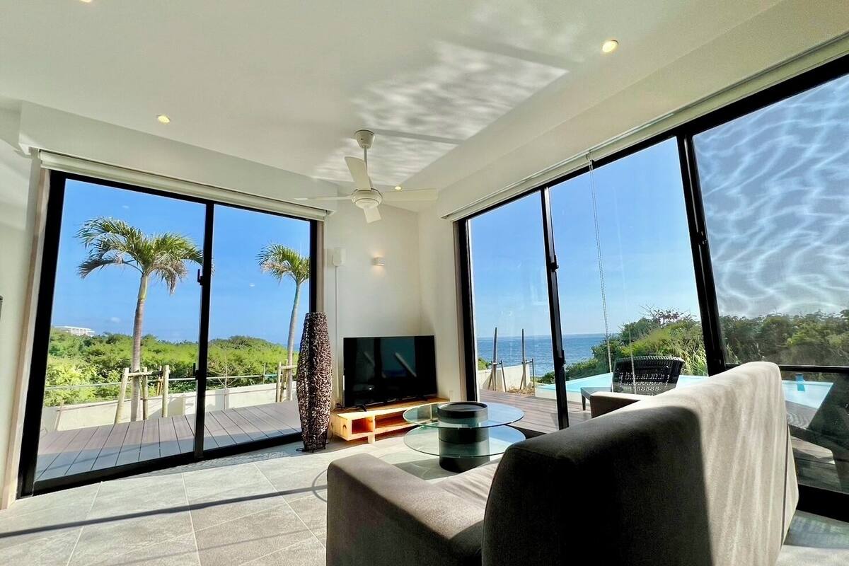 Una sala de estar moderna con ventanas amplias, un televisor de pantalla plana y una mesa de centro de vidrio.