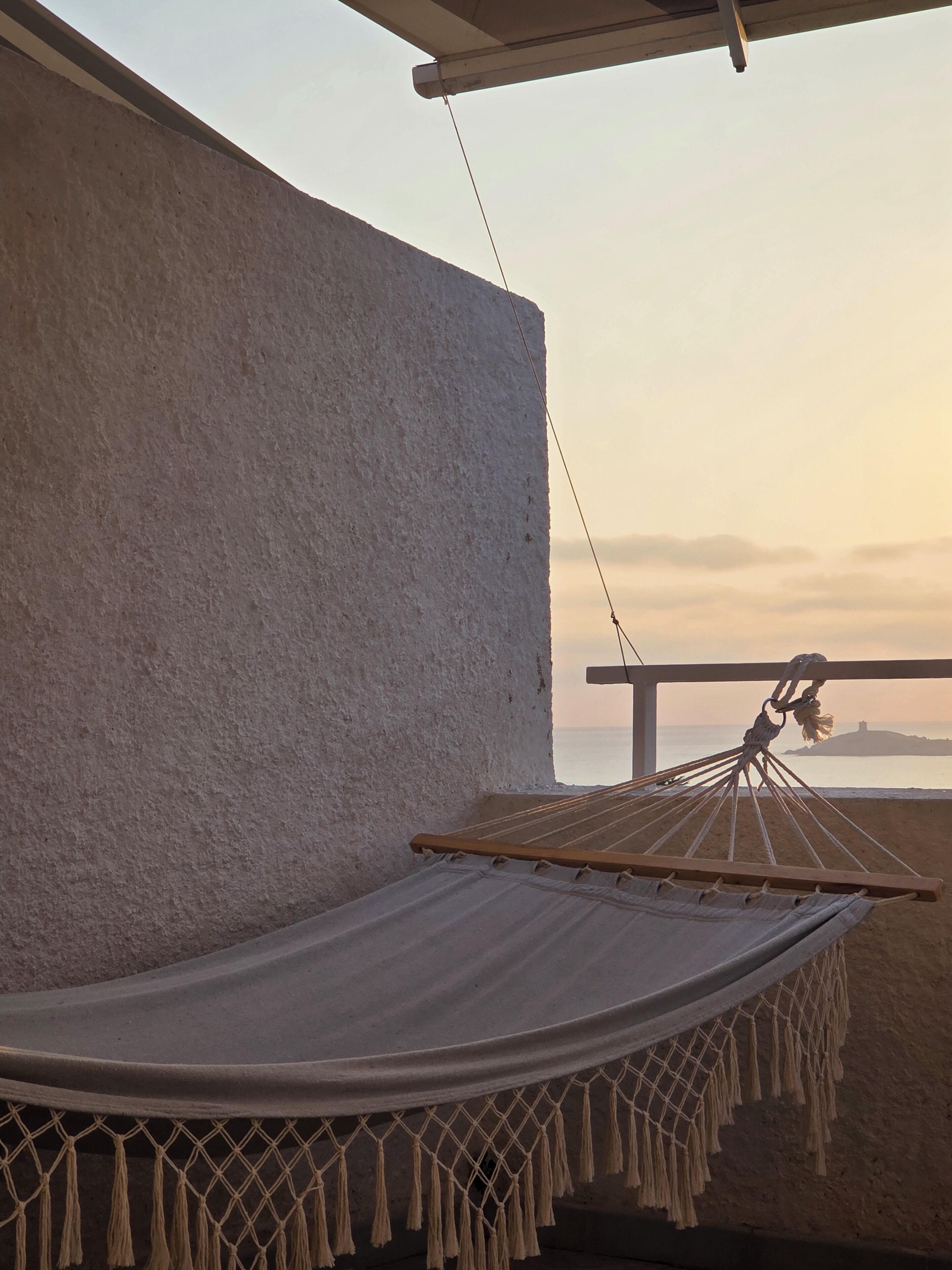 A hammock tied to a balcony railing overlooking a beach.
