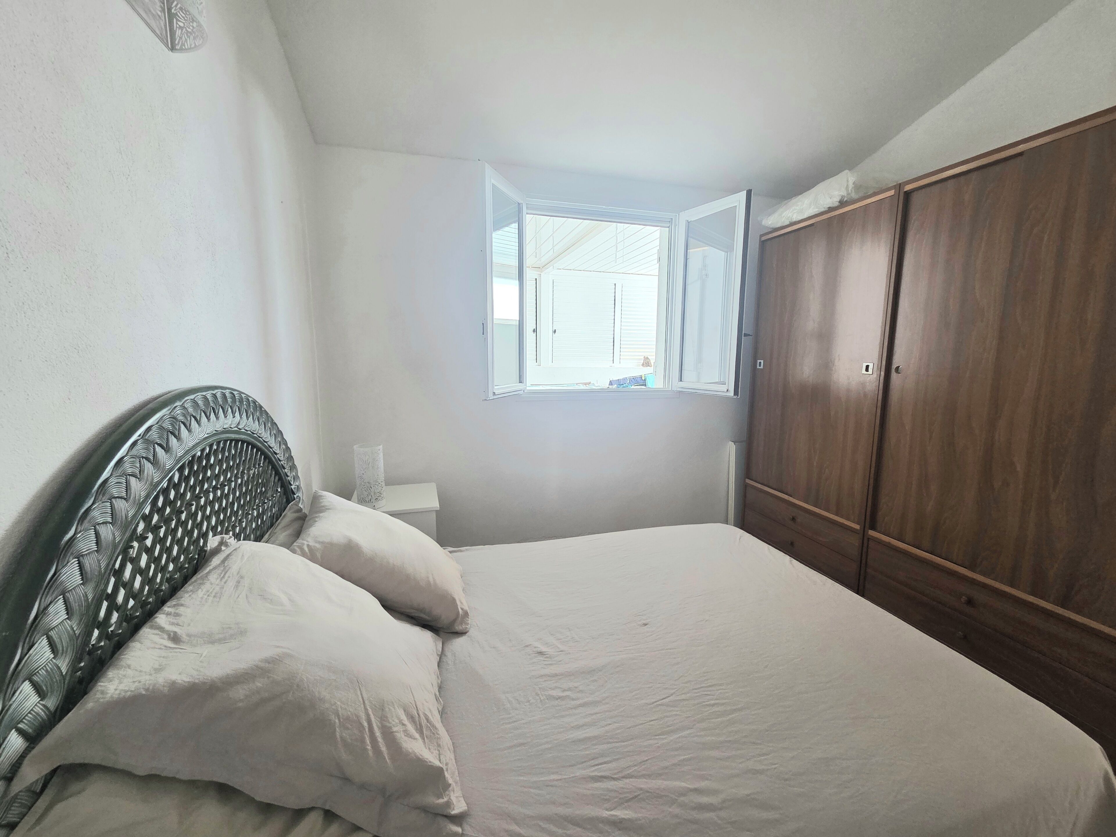 A bedroom with a bed, a wardrobe, a window, and a nightstand.