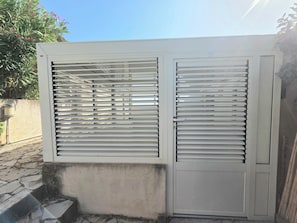 Una reja metálica blanca con listones horizontales, una base de concreto y el número 57 en el lado derecho.