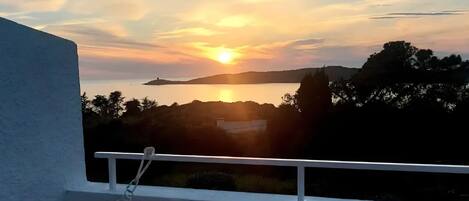 A balcony with a view of a sunset over a body of water and distant hills.