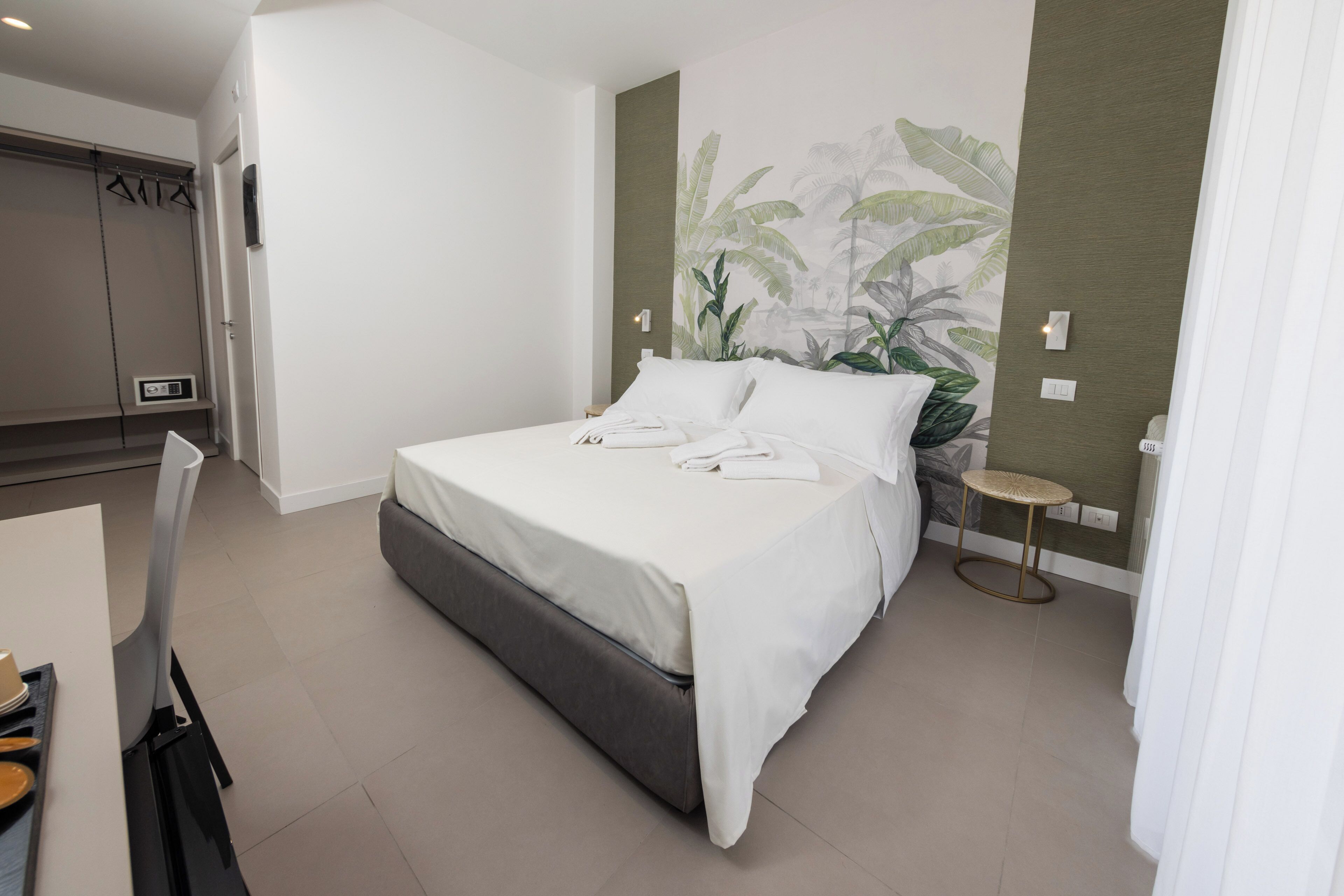Una habitación de hotel moderna con una cama grande, una mesita redonda y una planta en la pared.
