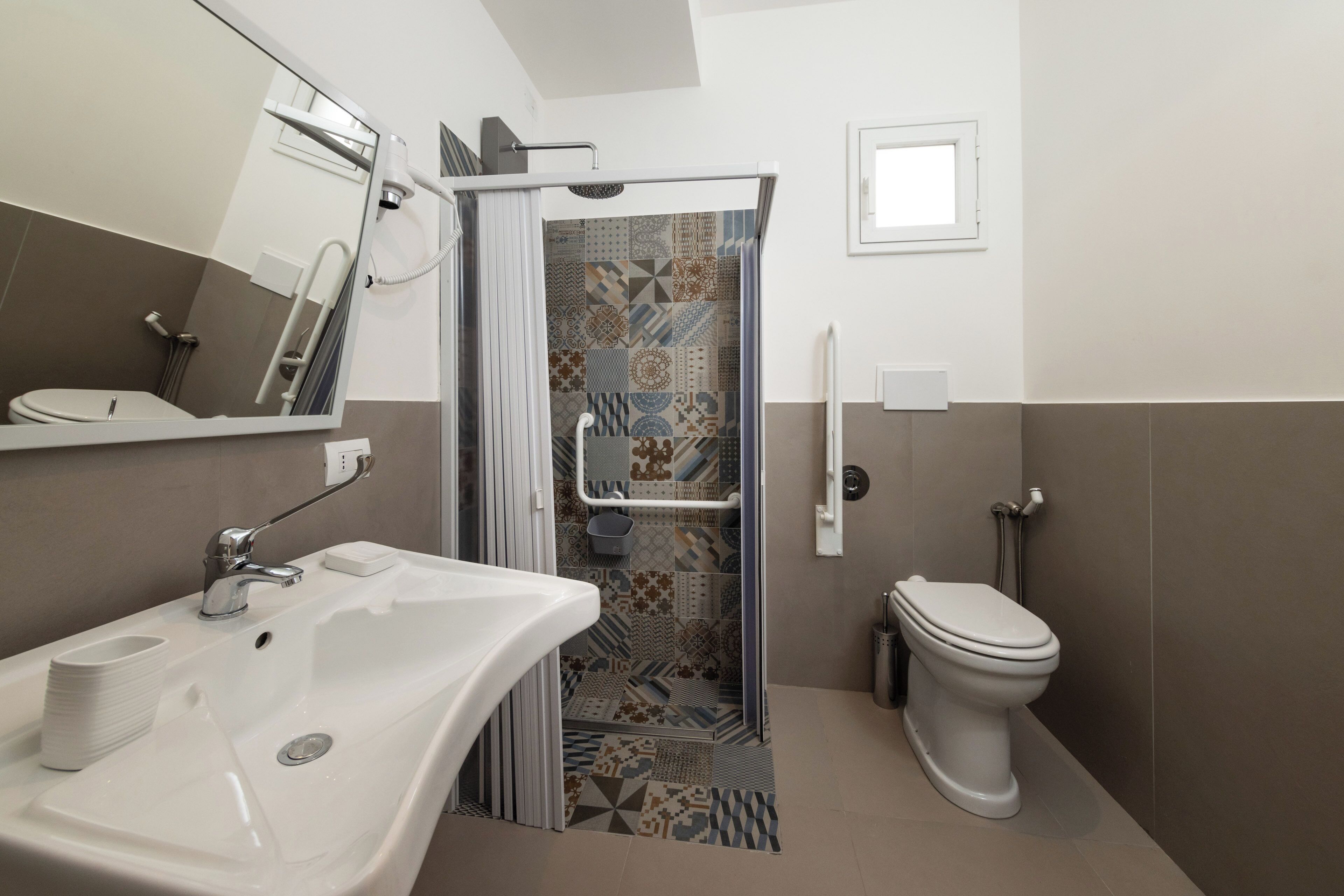 A bathroom with a white sink, a toilet, a shower with a glass door, and patterned tiles.