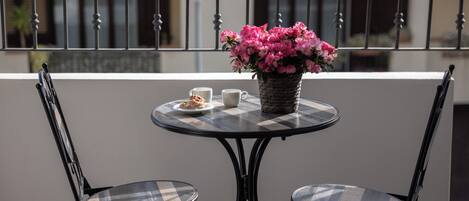 Una mesa redonda con dos sillas en un balcón. Hay una planta en maceta con flores rosadas sobre la mesa.