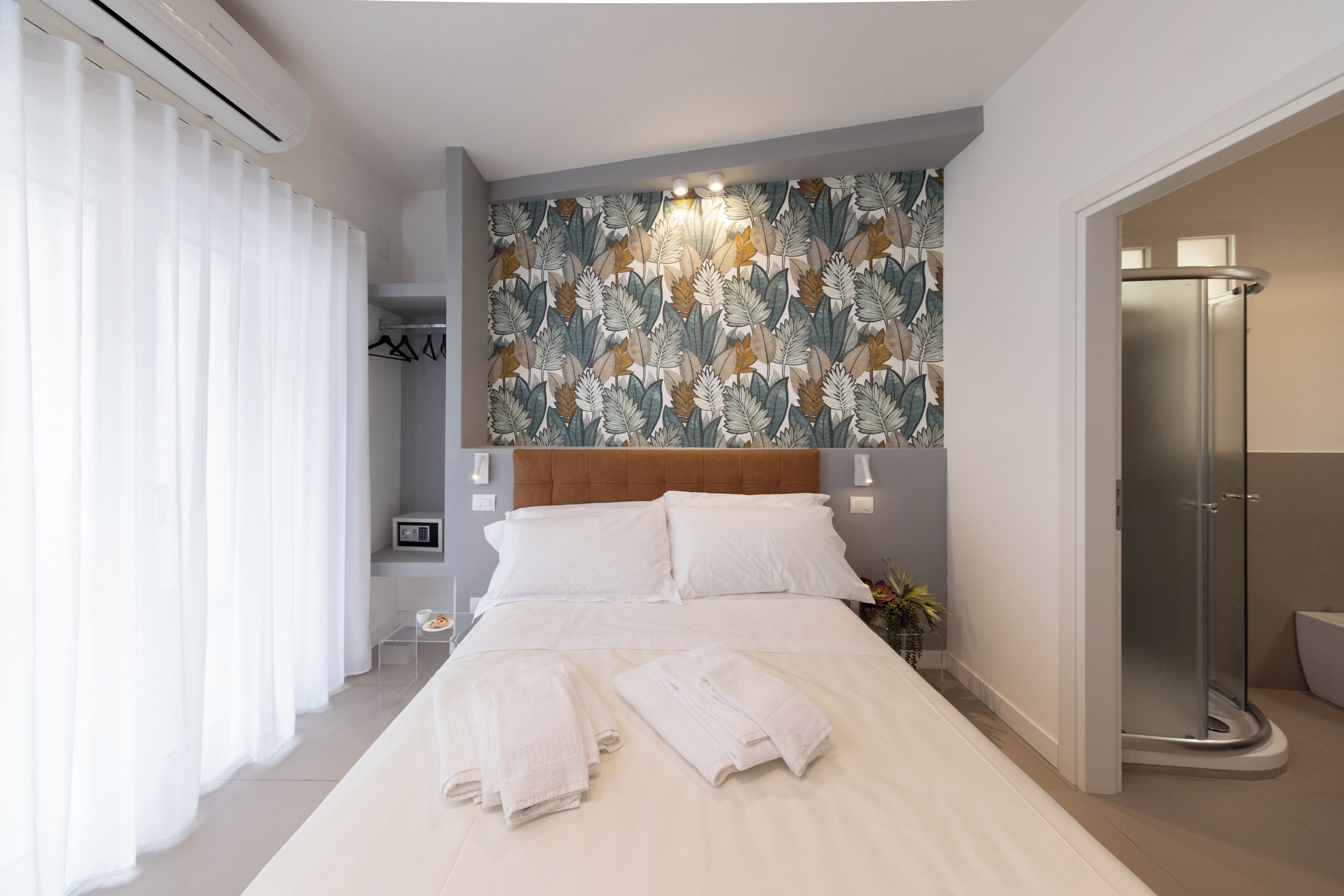 A hotel room with a large bed, white linens, a shower, and a floral-patterned wall.
