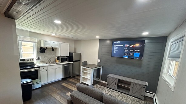 Un espace de vie compact comprenant un coin cuisine, un téléviseur à écran plat fixé au mur et un canapé gris.