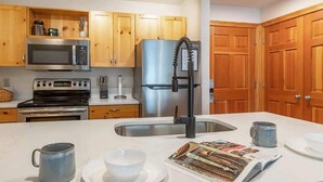 A kitchen with wooden cabinets, a stainless steel refrigerator, a microwave, and a sink.
