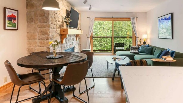 A living room with a stone wall, a round dining table, a sofa, and a large window.