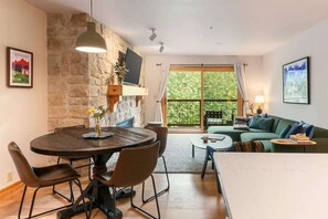A living room with a stone wall, a round dining table, a sofa, and a large window. - Basecamp Stays: Tranquil Retreat, Hot Tub, Shuttle (Driggs)