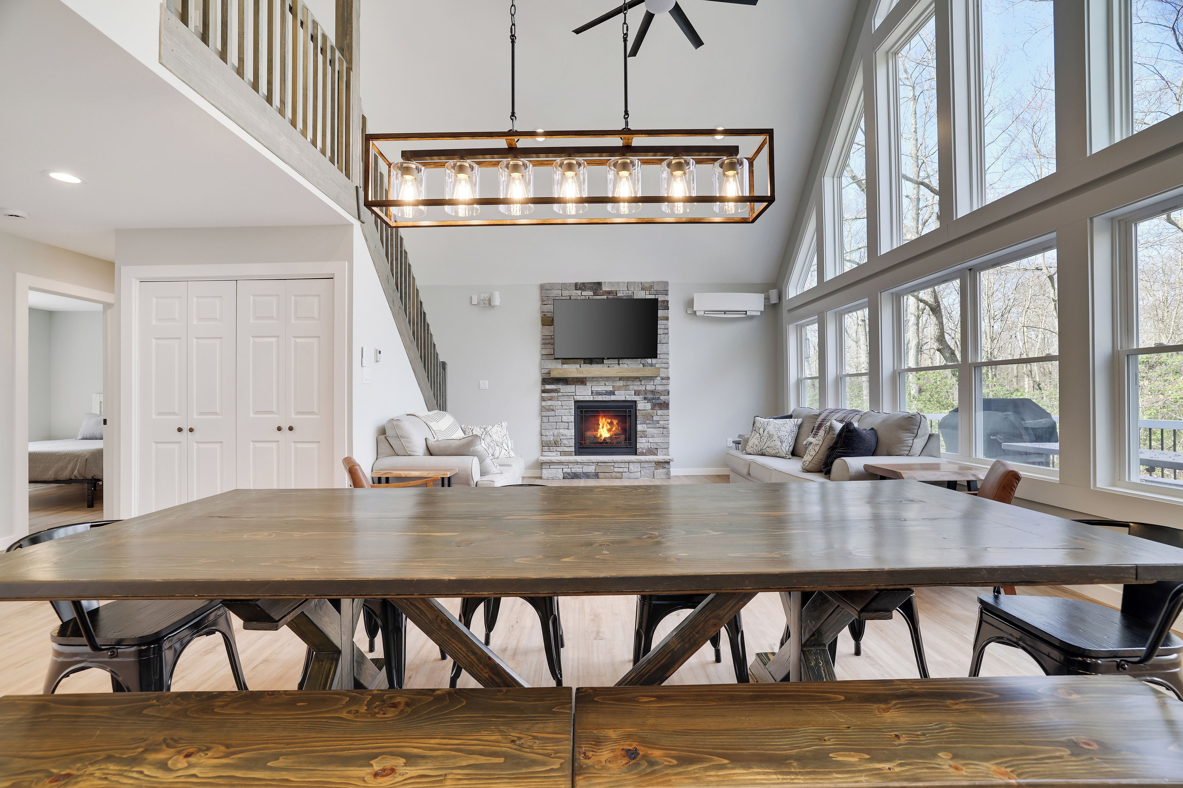 A spacious living room with a large wooden dining table, a fireplace, and a high ceiling with a fan.
