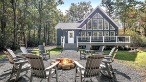 A cabin with a deck, surrounded by Adirondack chairs, and a fire pit in the center. - Lake & Beach + Firepit + King Beds + Swing set (Jim Thorpe)