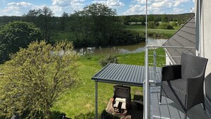 A patio with a view of a river and forest, a metal pergola, and two wicker chairs. - Neue , Moderne , Lichtdurchflutete Ferienwohnung 🌸 (Hallerndorf)