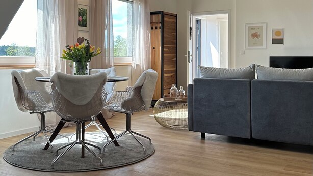 A modern living room with a dining area, wooden ceiling beams, a grey sofa, and a round rug. - Neue , Moderne , Lichtdurchflutete Ferienwohnung 🌸 (Hallerndorf)
