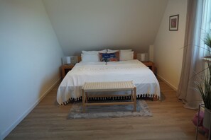 A bedroom with a bed, bedside tables, a bench, a rug, and a potted plant. - Neue , Moderne , Lichtdurchflutete Ferienwohnung 🌸 (Hallerndorf)