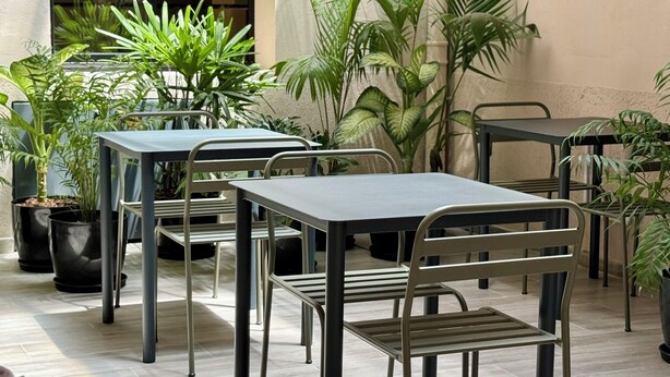 En udendørs terrasse med metalborde og -stole, omgivet af krukker med planter.