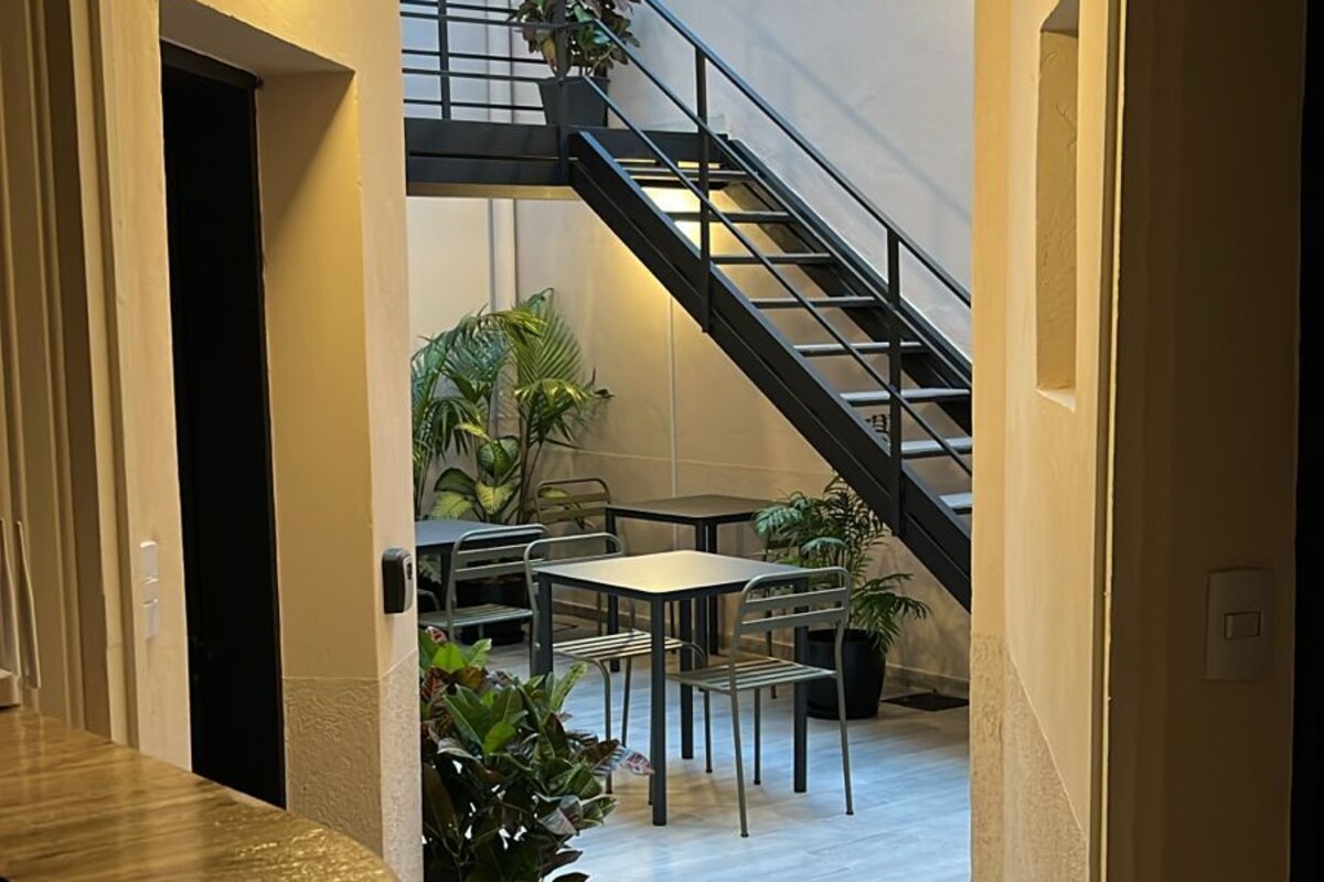 A modern interior with a staircase leading to an upper level, a dining area with tables and chairs, and potted plants.