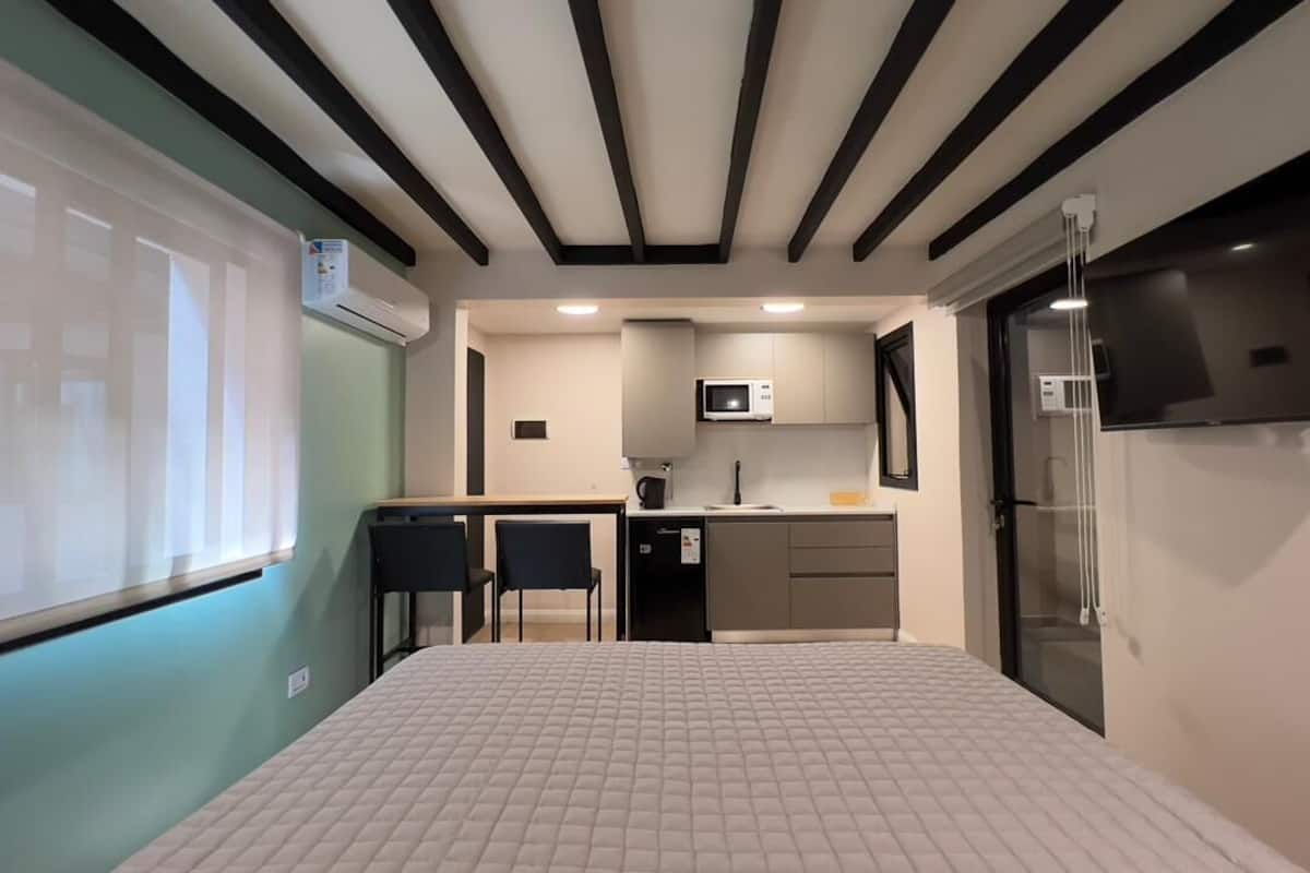 A compact hotel room with a kitchenette, a bed, a desk, and a TV.
