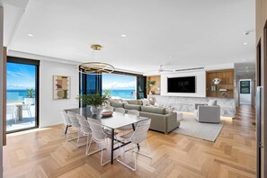 Un espace de vie moderne comprenant un coin repas, un ensemble de canapés, un téléviseur à écran plat et une vue sur la mer.