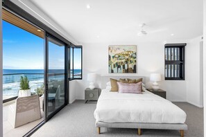 Une chambre avec un grand lit, un tableau, une fenêtre donnant sur la mer et un balcon avec une chaise et une plante.