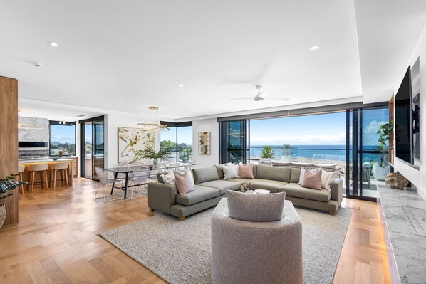 A spacious living area with a large sofa, a dining table, and a view of the sea.