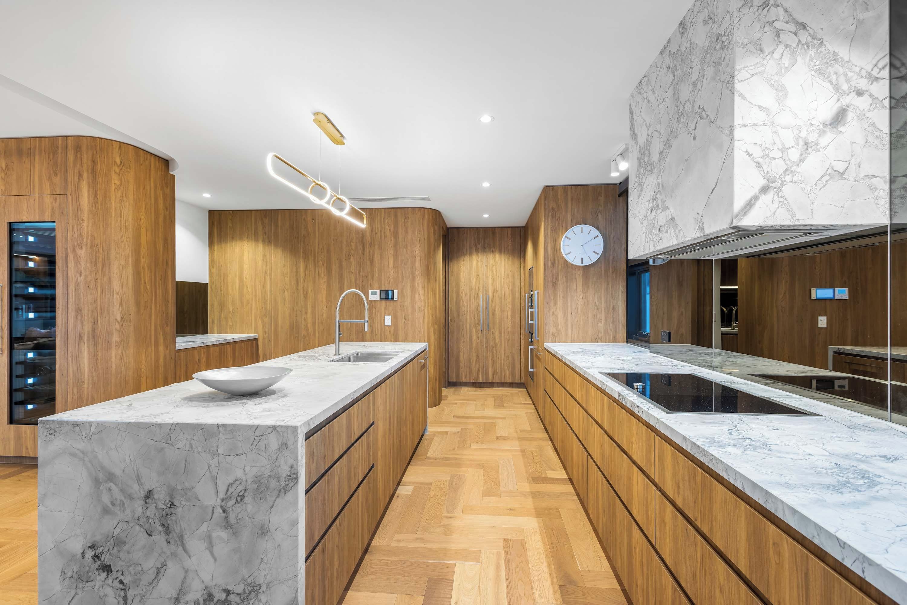 A modern kitchen with wooden cabinetry, marble countertops, and a built-in oven.