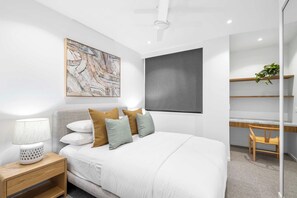 A modern bedroom with a bed, bedside table, lamp, and a large abstract painting. - Penthouse First Bay Coolum (Coolum Beach)