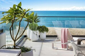 A rooftop terrace with a view of the sea, featuring potted plants, lounge chairs, and a white railing. - Penthouse First Bay Coolum (Coolum Beach)